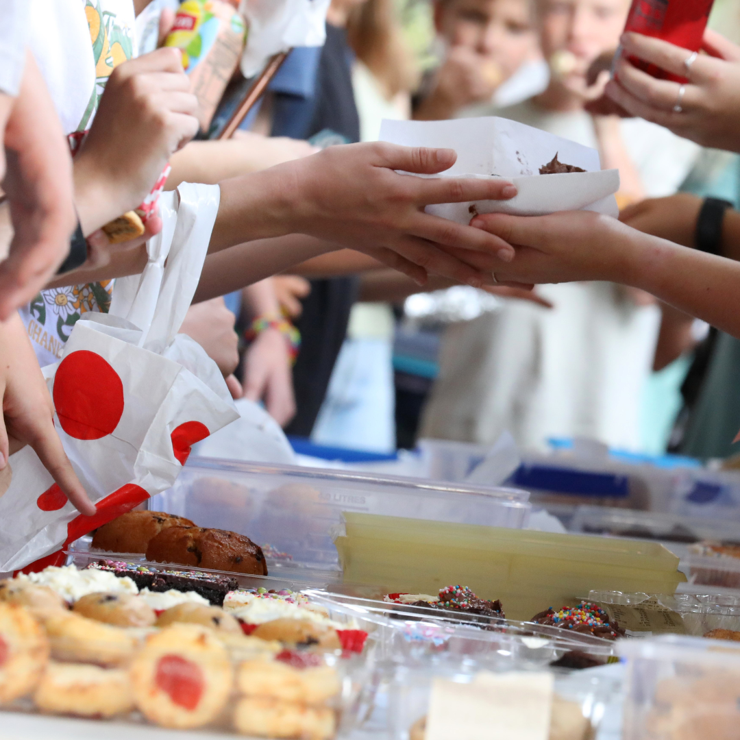 Hands exchanging baked goods at a crowded vendor table, with cookies, pastries, and desserts in view.