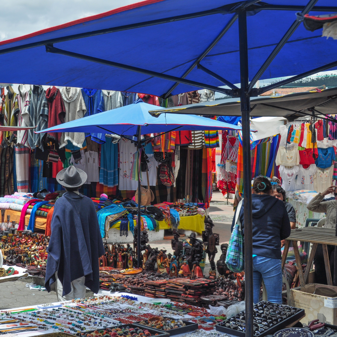 Outdoor vendor booths with colorful handmade textiles, crafts, and clothing on display.