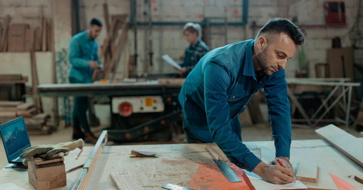An entrepreneur in a workshop drafting plans with a ruler and pencil at a work table. An entrepreneur in a workshop drafting plans with a ruler and pencil at a work table.